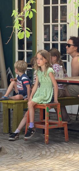 A group of adults and children are casually seated outdoors on a sunny afternoon at Haarweg, Vuren